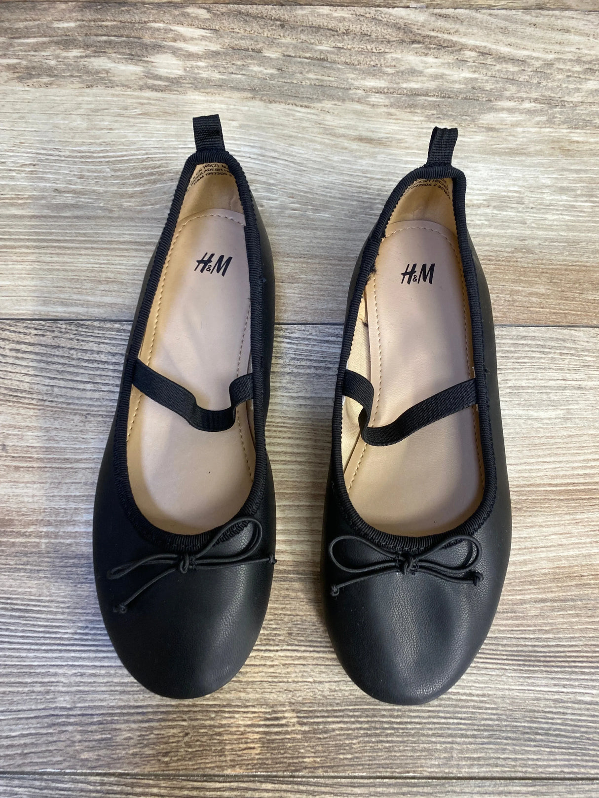 Top-down view of H&M Mary Jane bow flats showcasing front bow and elastic strap on wood floor