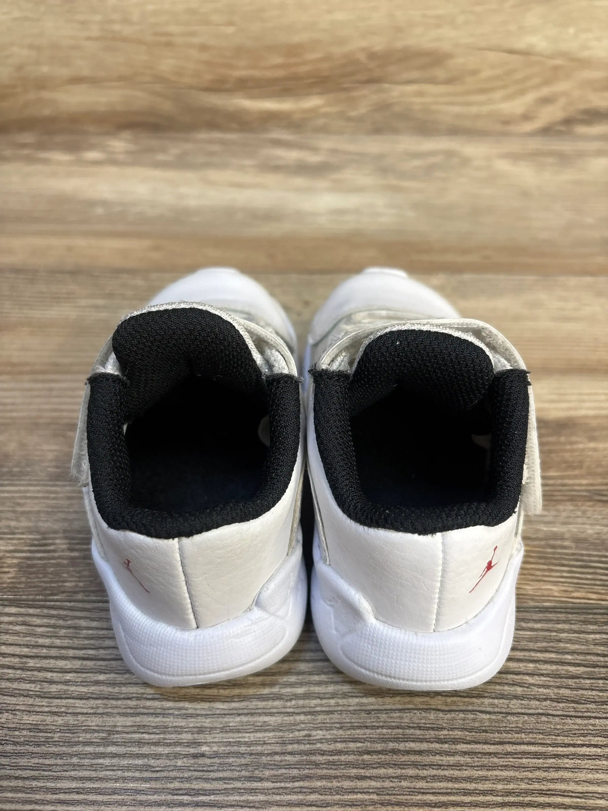 Pair of white toddler sneakers with black inner lining on wooden floor