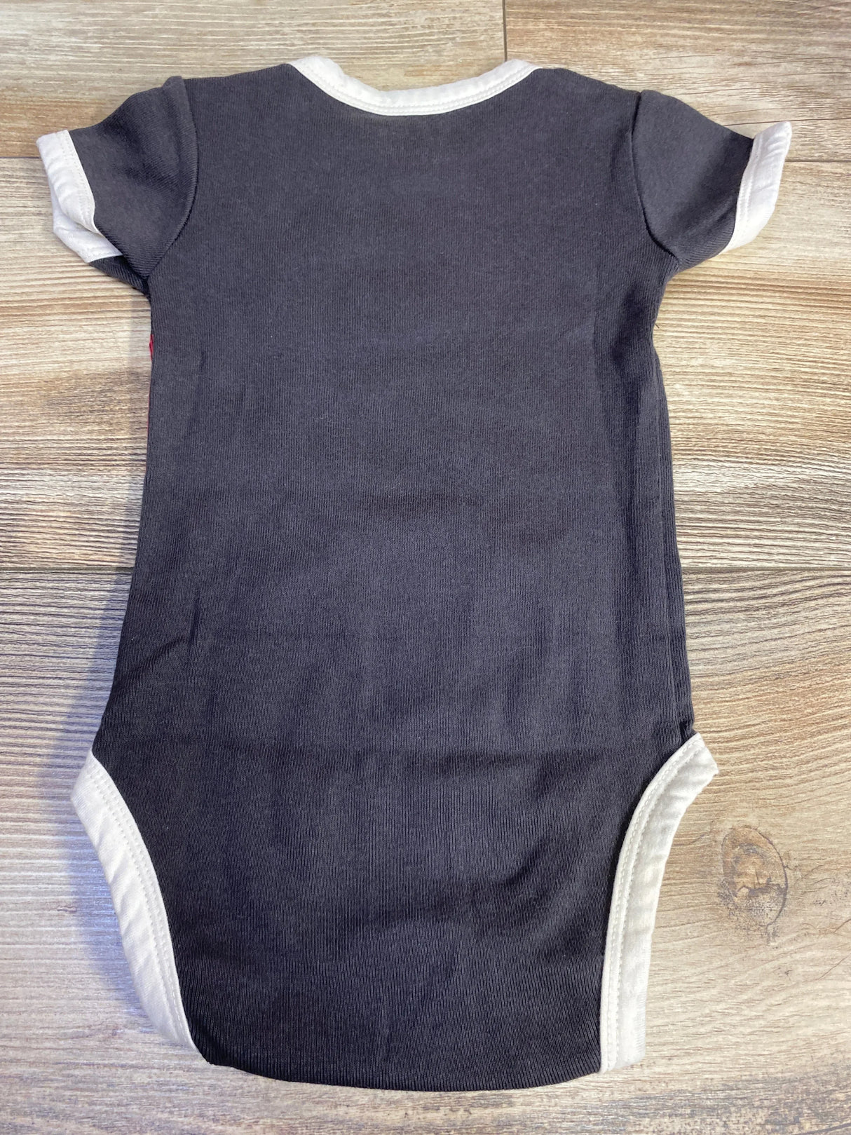 Black baby onesie with white trim laid flat on wooden surface