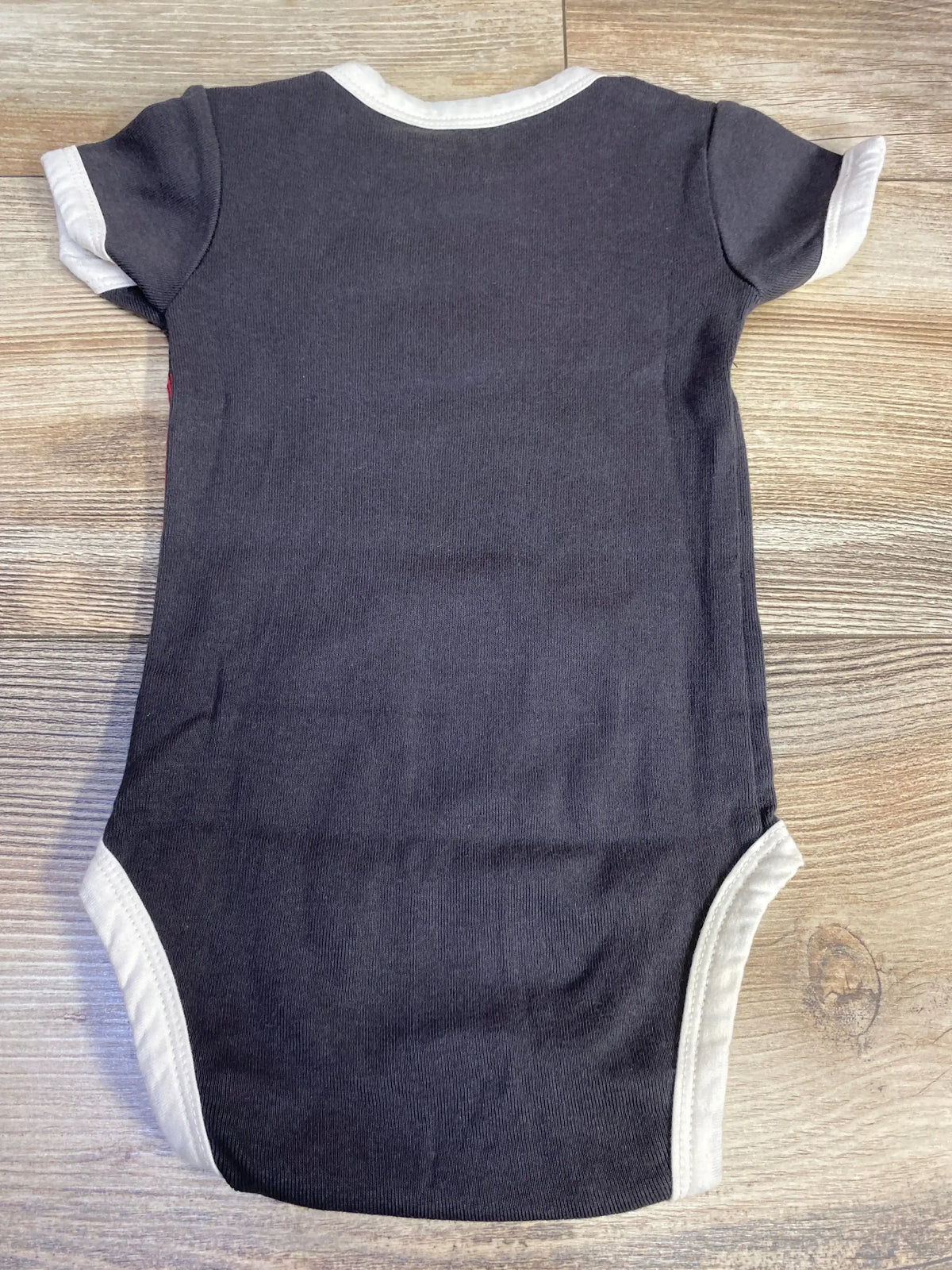Black baby onesie with white trim laid flat on wooden surface