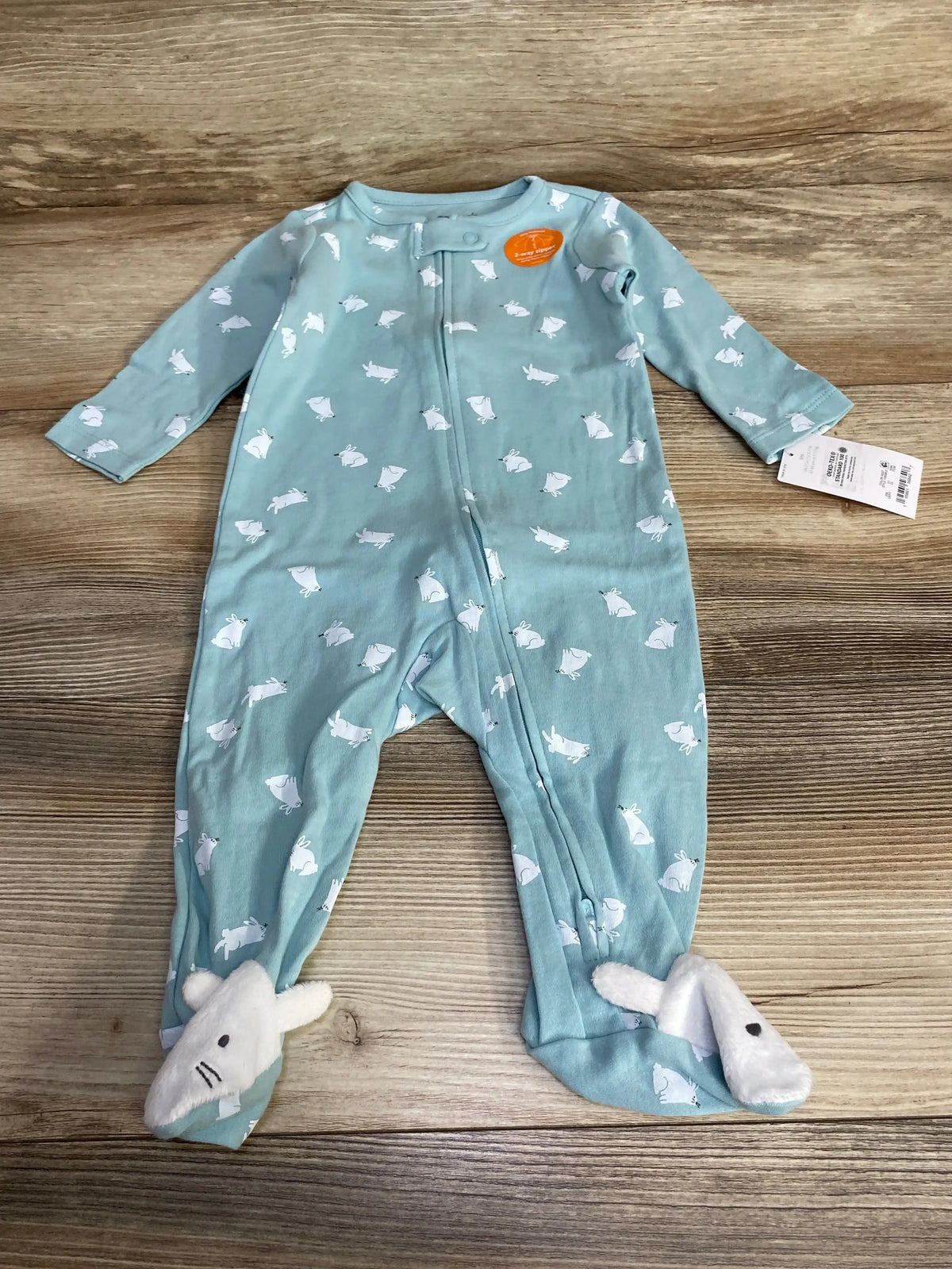 Flat lay of NEW Just One You bunny print sleeper size 6m showcasing light blue zip-up footed pajamas with white bunny print 3D bunny feet and hangtag on wood plank floor