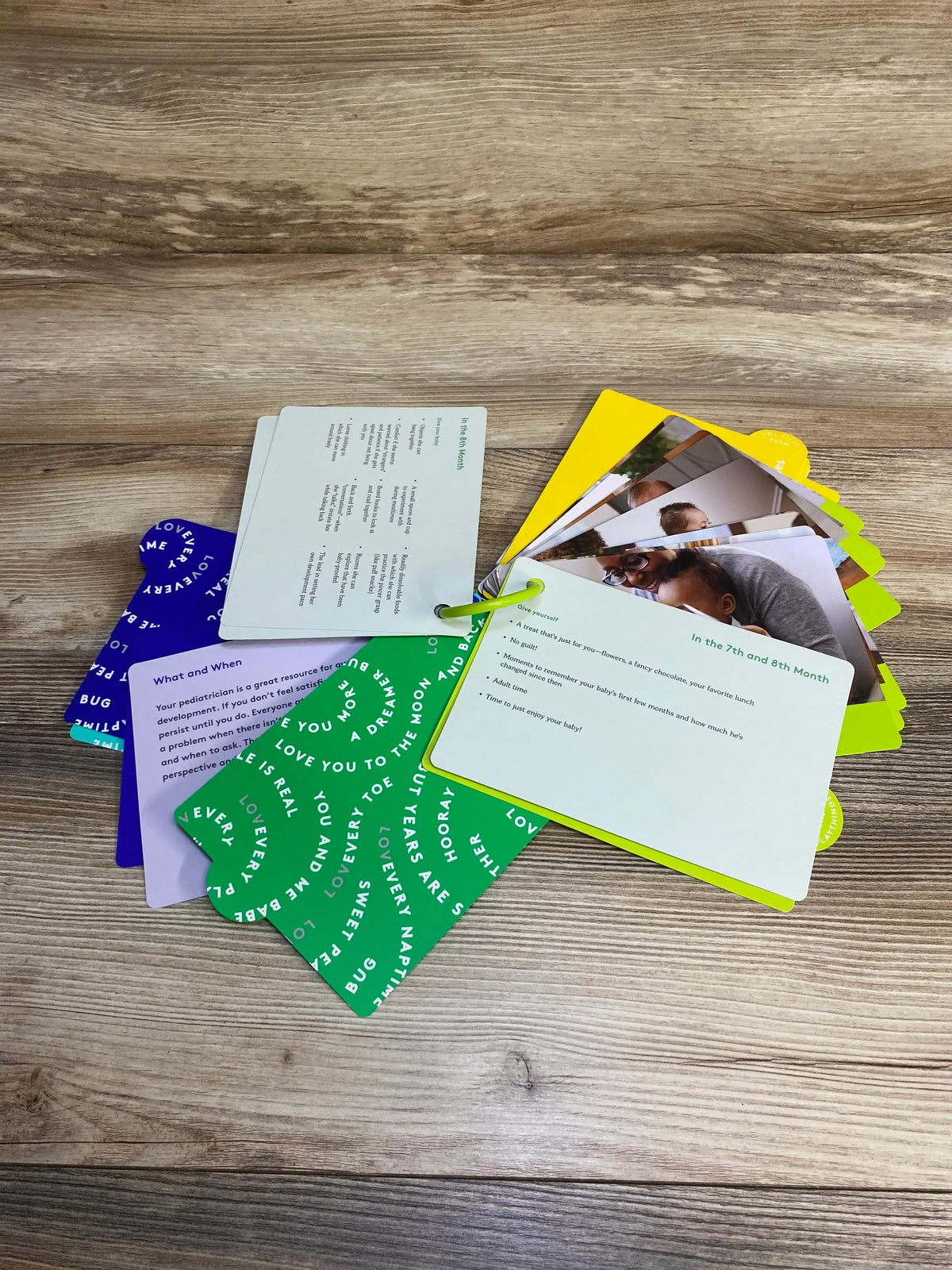 Angled view of Lovevery The Inspector Play Guide showcasing colorful ring-bound activity cards with photos and parenting advice on a wood tabletop