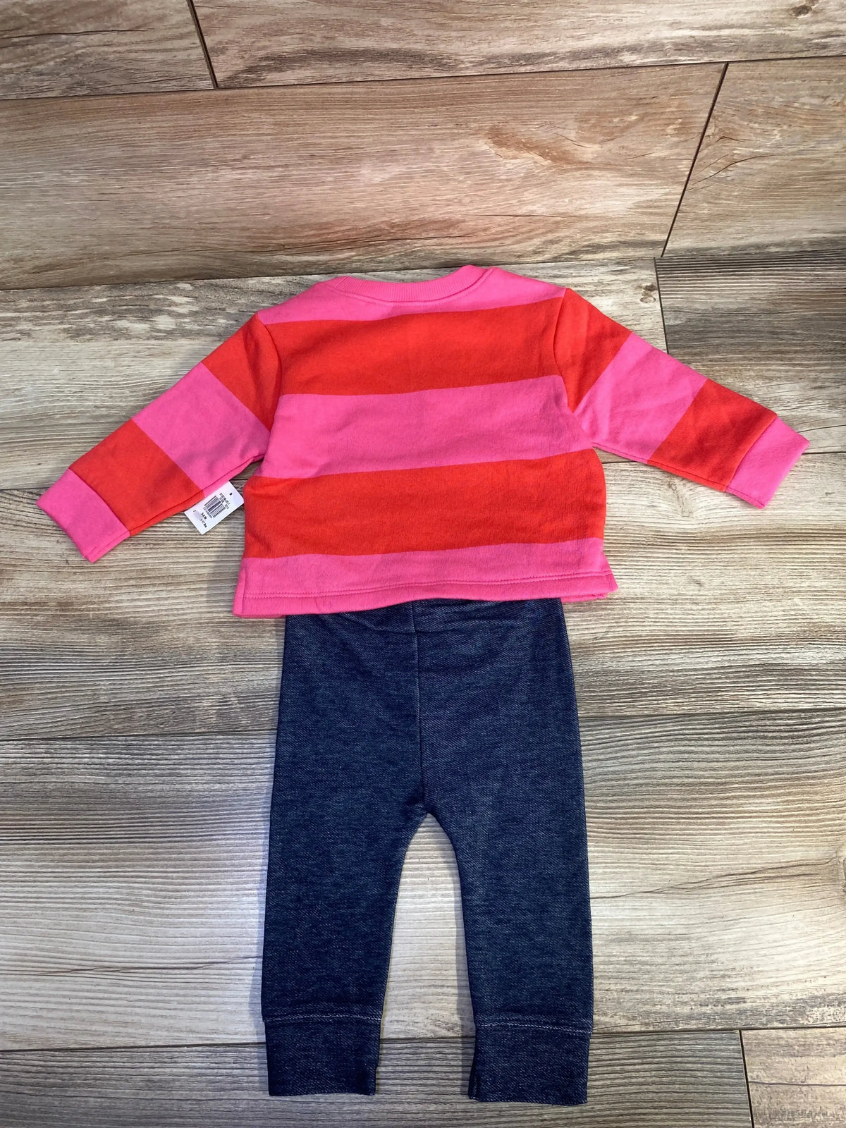 Infant outfit with pink and red striped long-sleeve shirt and dark gray leggings on wood floor