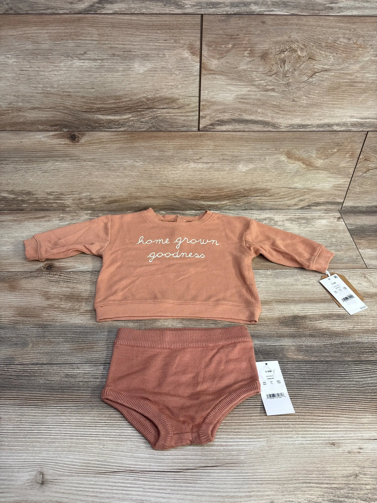 Orange baby outfit set with long sleeve top reading 'home grown goodness' and matching bottoms on wood floor