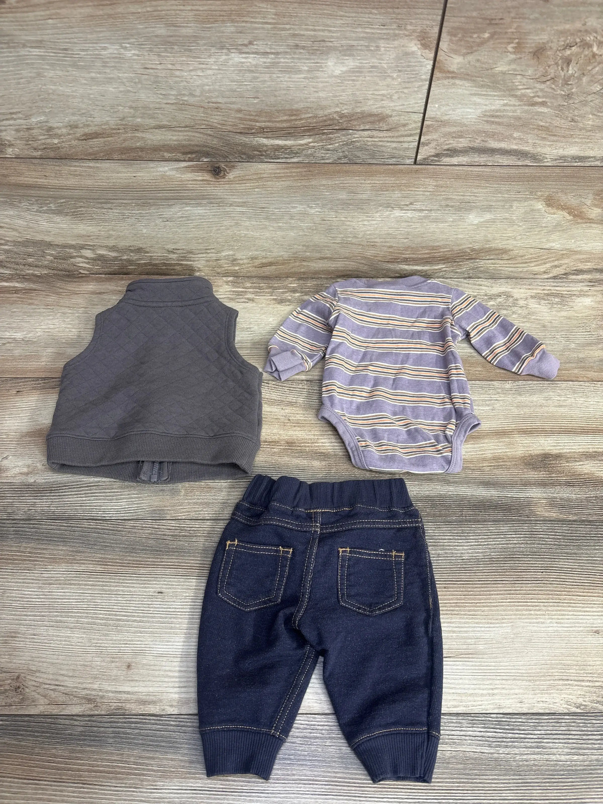 Baby outfit set with striped long sleeve bodysuit, gray vest, and denim pants on wood floor