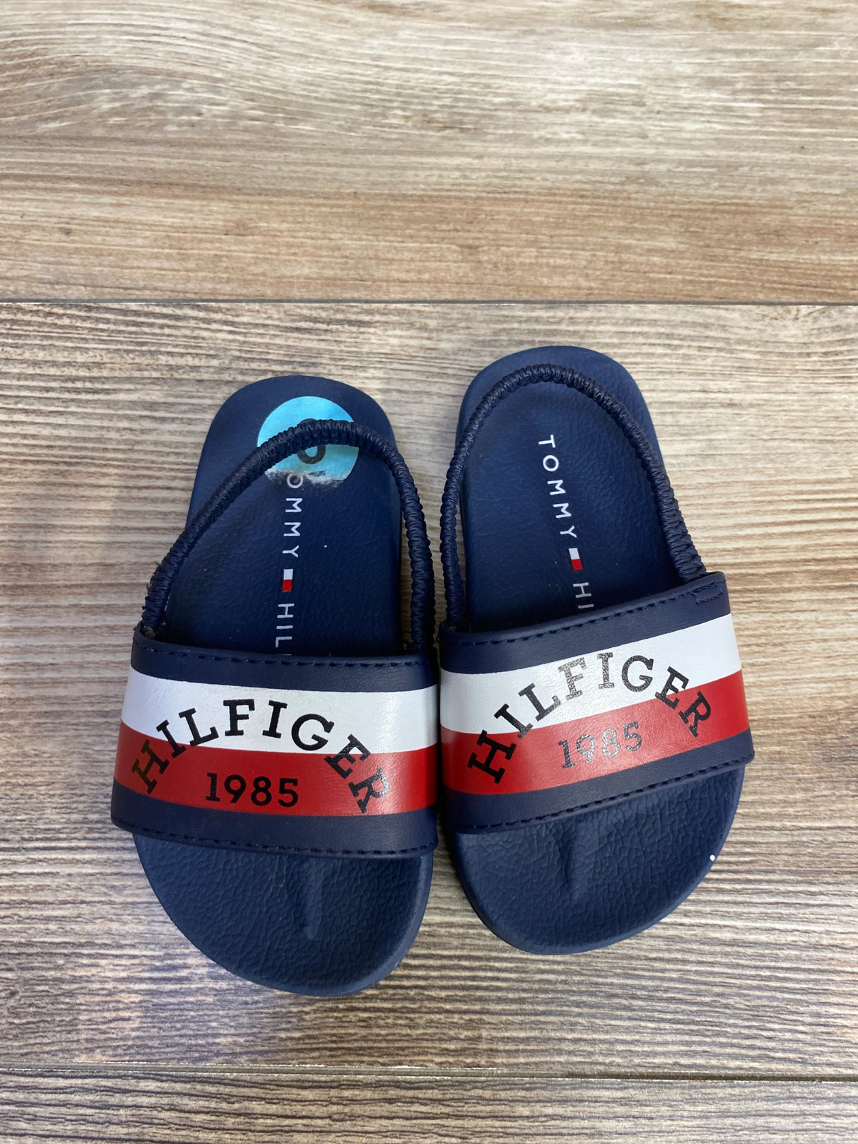 Tommy Hilfiger baby sandals navy blue with red and white stripes, wood background