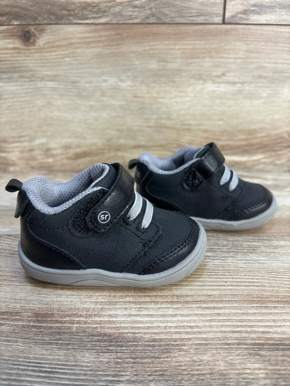 Black toddler sneakers with gray soles and velcro straps on wood background