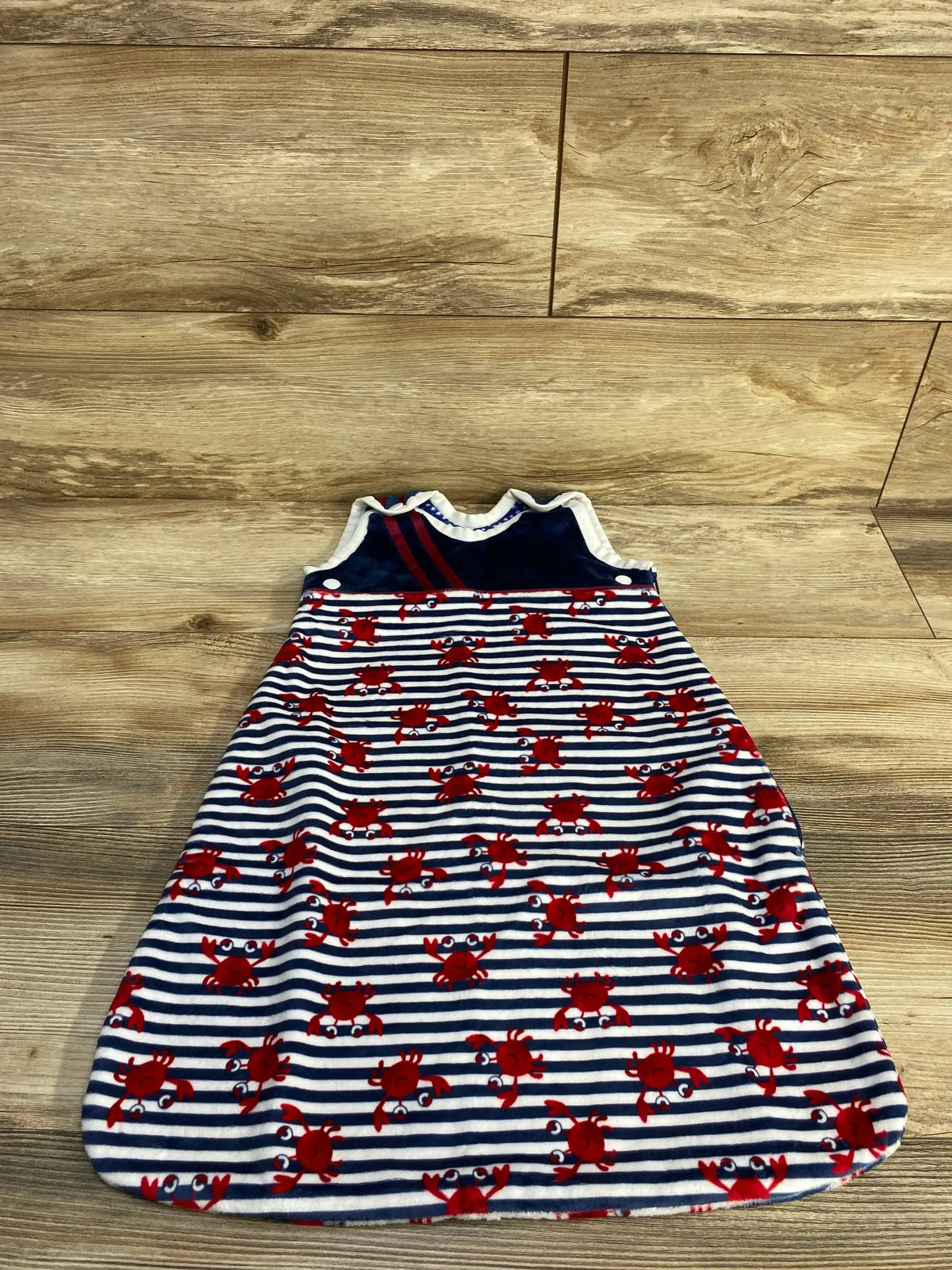 Top view of navy and white newborn sleep sack with red crab print, sleeveless A line with snap closures on wood background