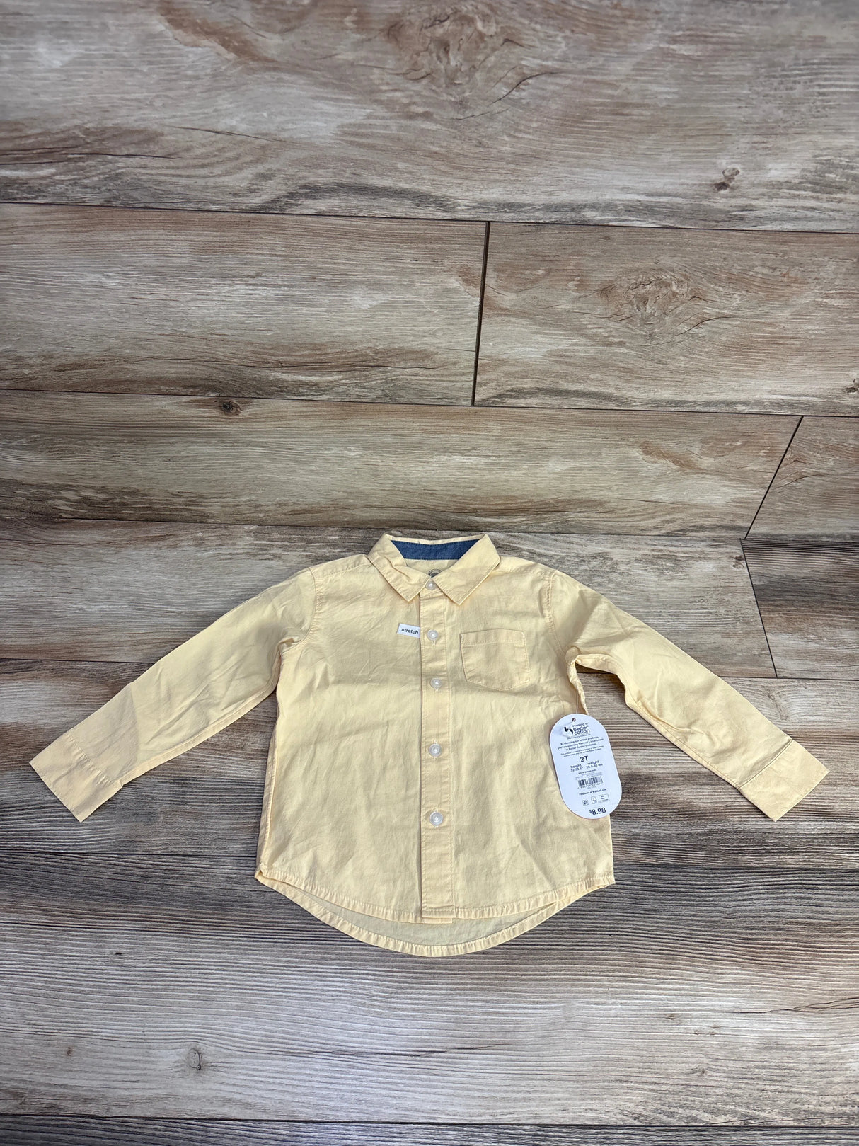 Yellow long-sleeve toddler shirt with collar and front pocket on wooden floor, size 2T