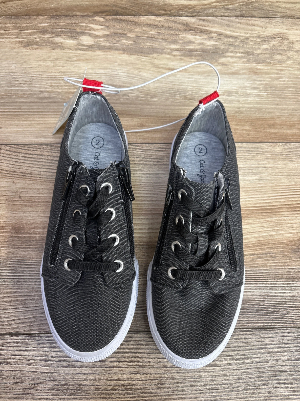 Top view of NEW Cat and Jack Lucian double zipper sneakers grey sz 2Y showcasing canvas upper white sole and side zippers with hangtags on wood plank floor