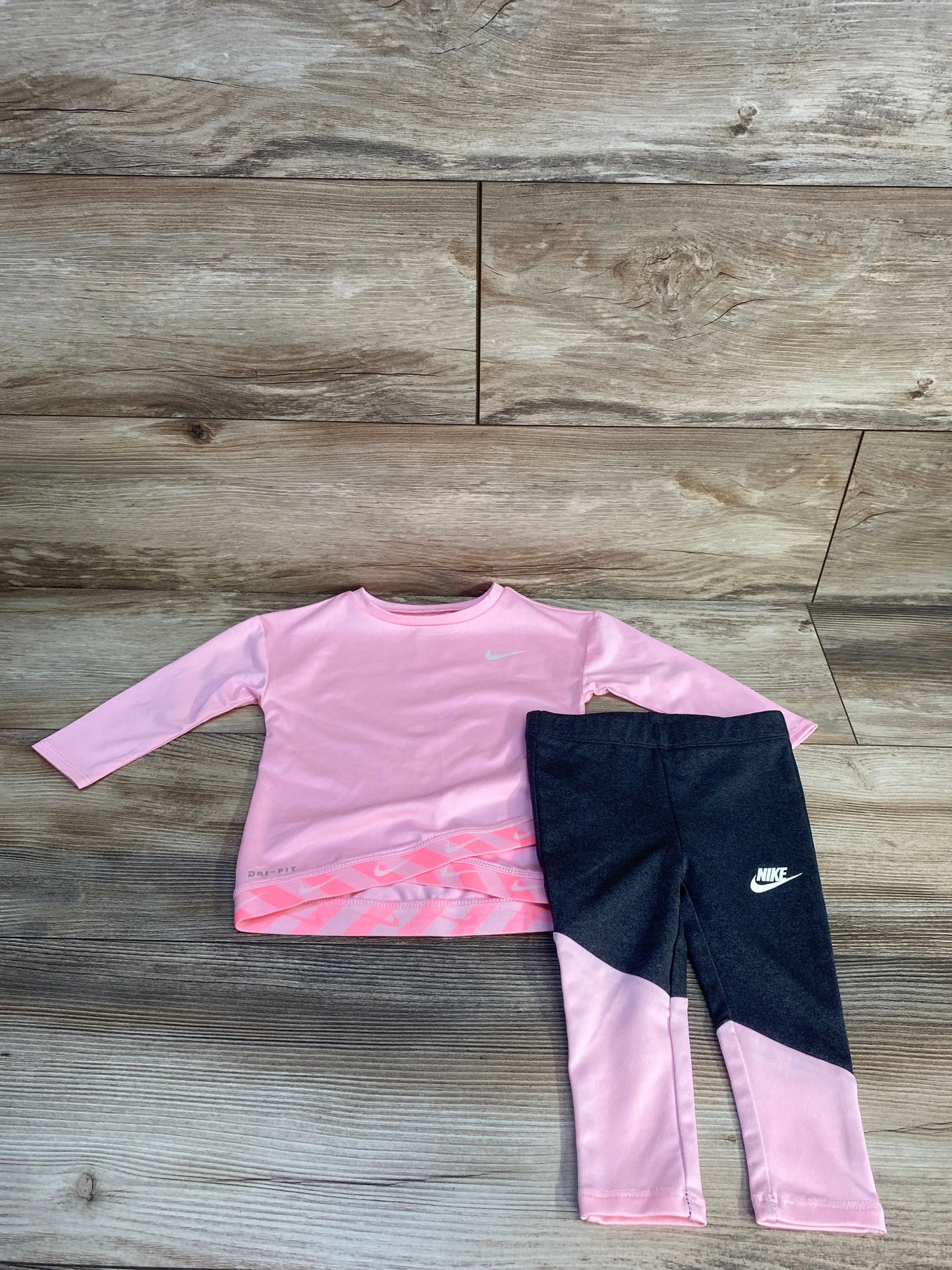 Pink Nike Dri-FIT long sleeve shirt and black leggings kids outfit on wood floor