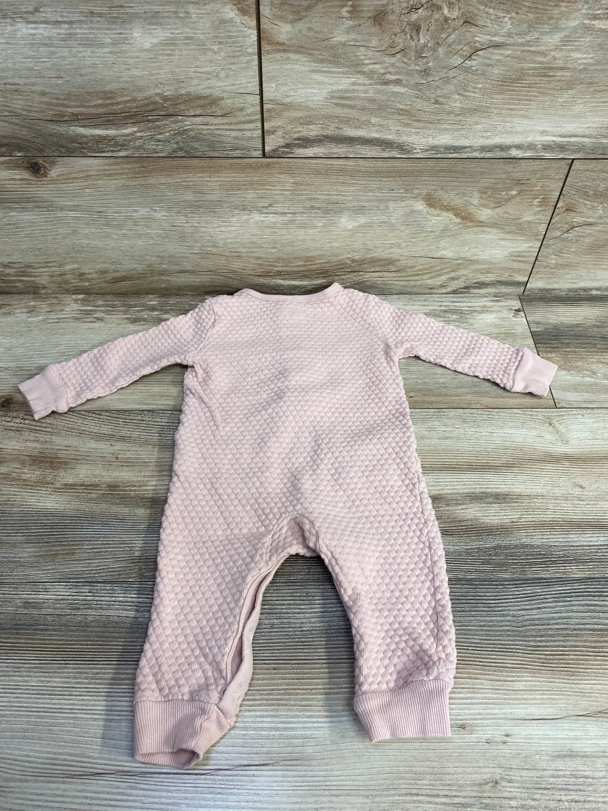 Pink textured baby romper with long sleeves displayed on wooden floor