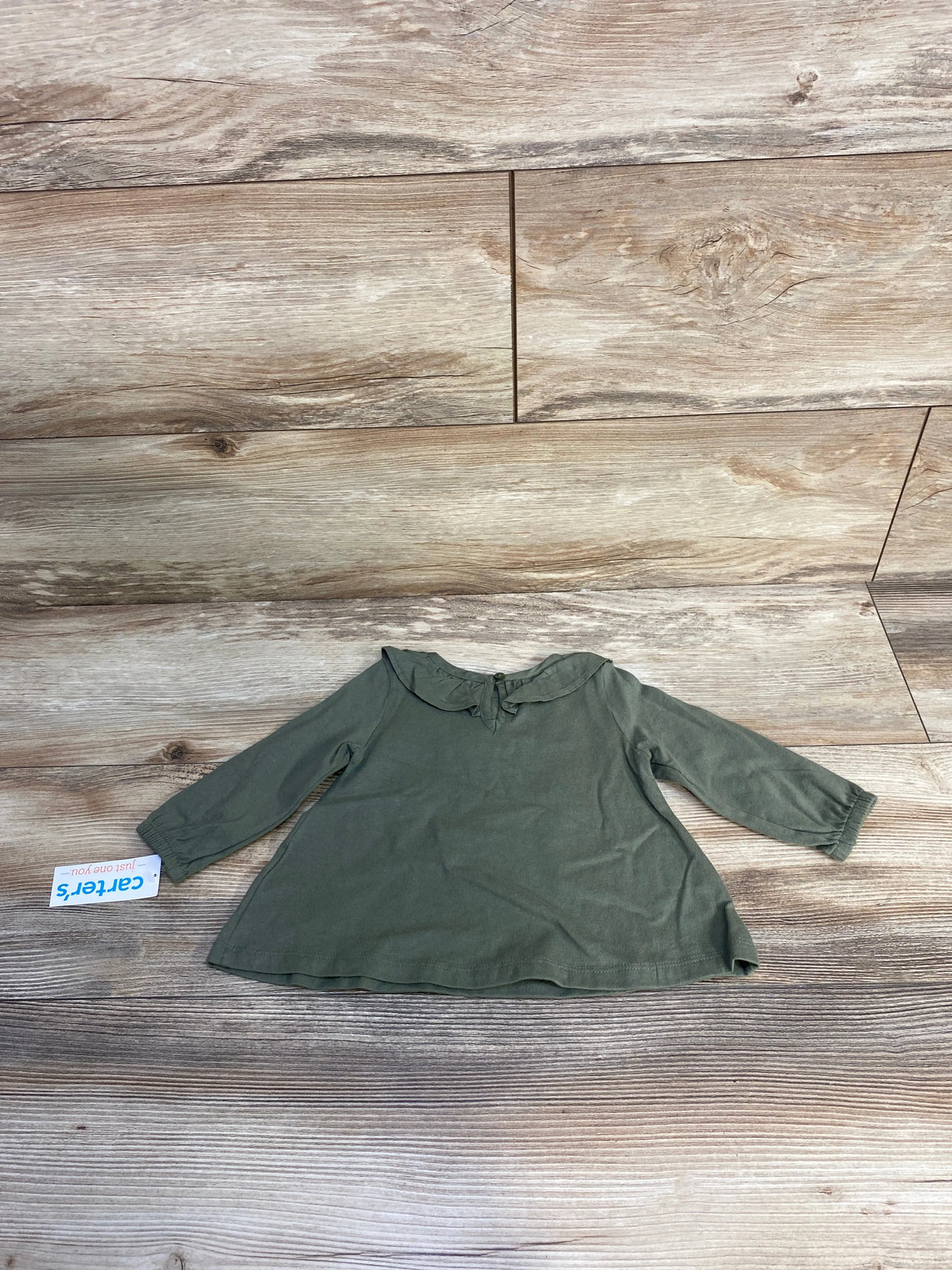 Olive green long sleeve baby top with ruffled collar on wood floor, Carter's tag visible
