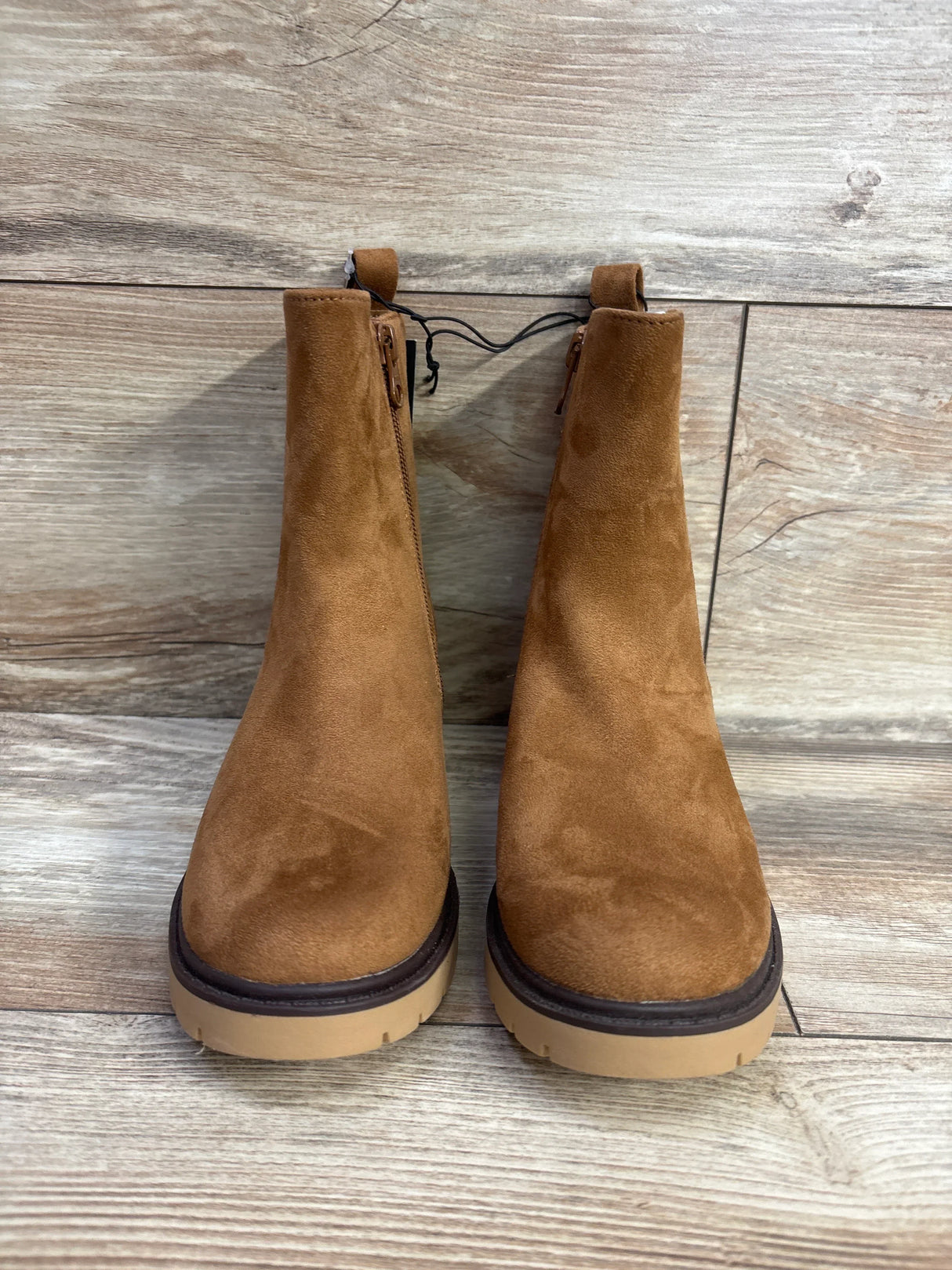 Pair of brown suede kids boots with side zippers on wood floor background