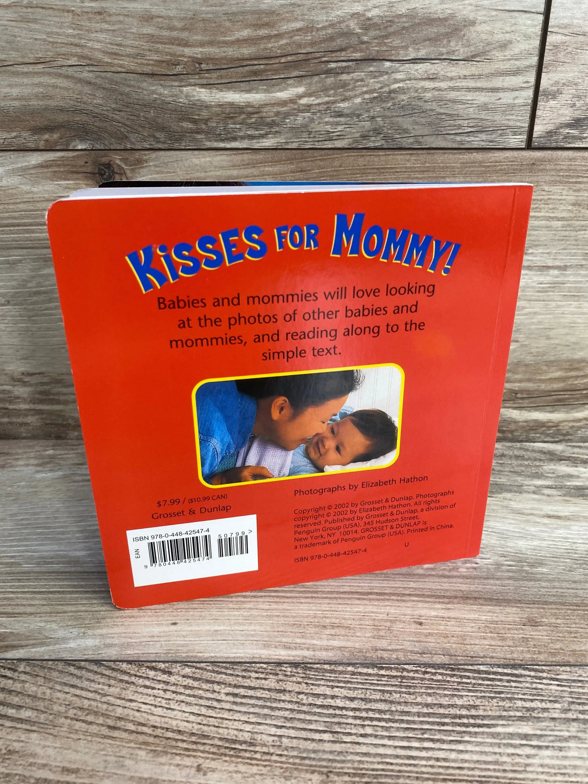 Back of Kisses for Mommy! board book, red cover with large title, inset photo of mother kissing baby, barcode on wood surface