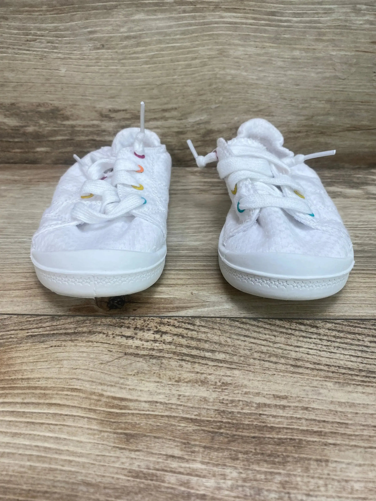 Front view of Wonder Nation girls' white bump-toe sneakers size 10C showing rainbow-colored eyelets and textured fabric on wood background