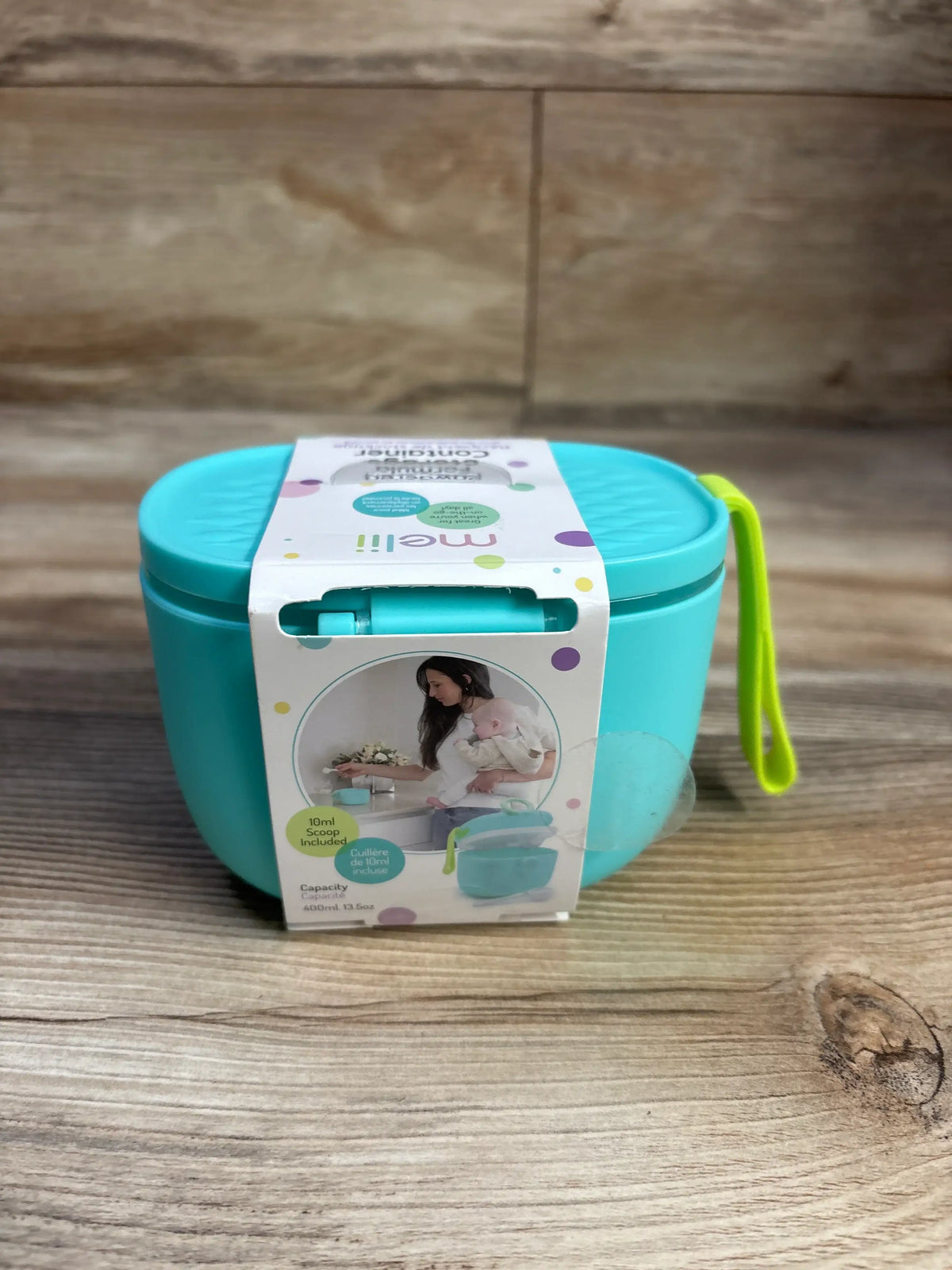 Front view of a turquoise Melii powdered formula storage container with included scoop and lime green handle on a wood surface