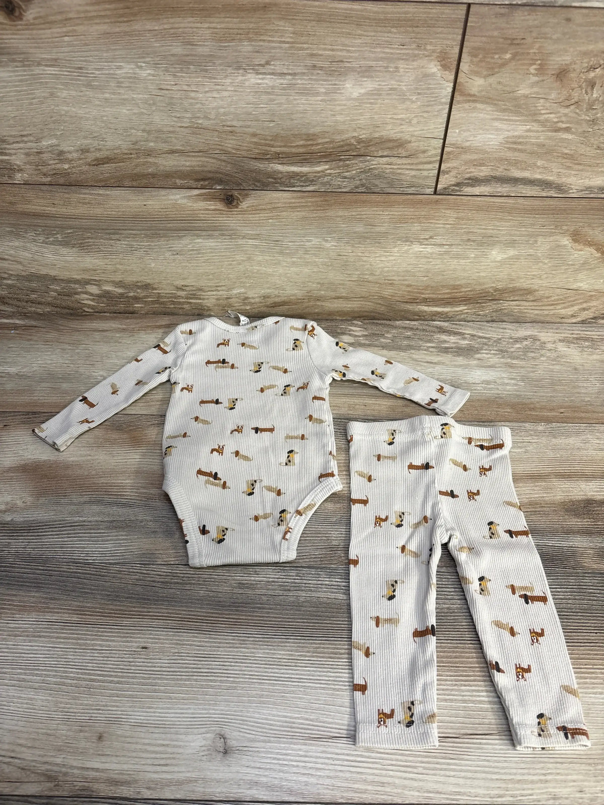 Flat lay of beige 2-piece ribbed baby bodysuit and matching leggings with small dog print on wood background