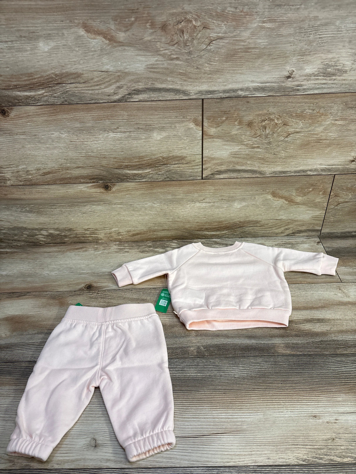 Light pink baby sweatpants and long-sleeve sweatshirt set on wooden floor background