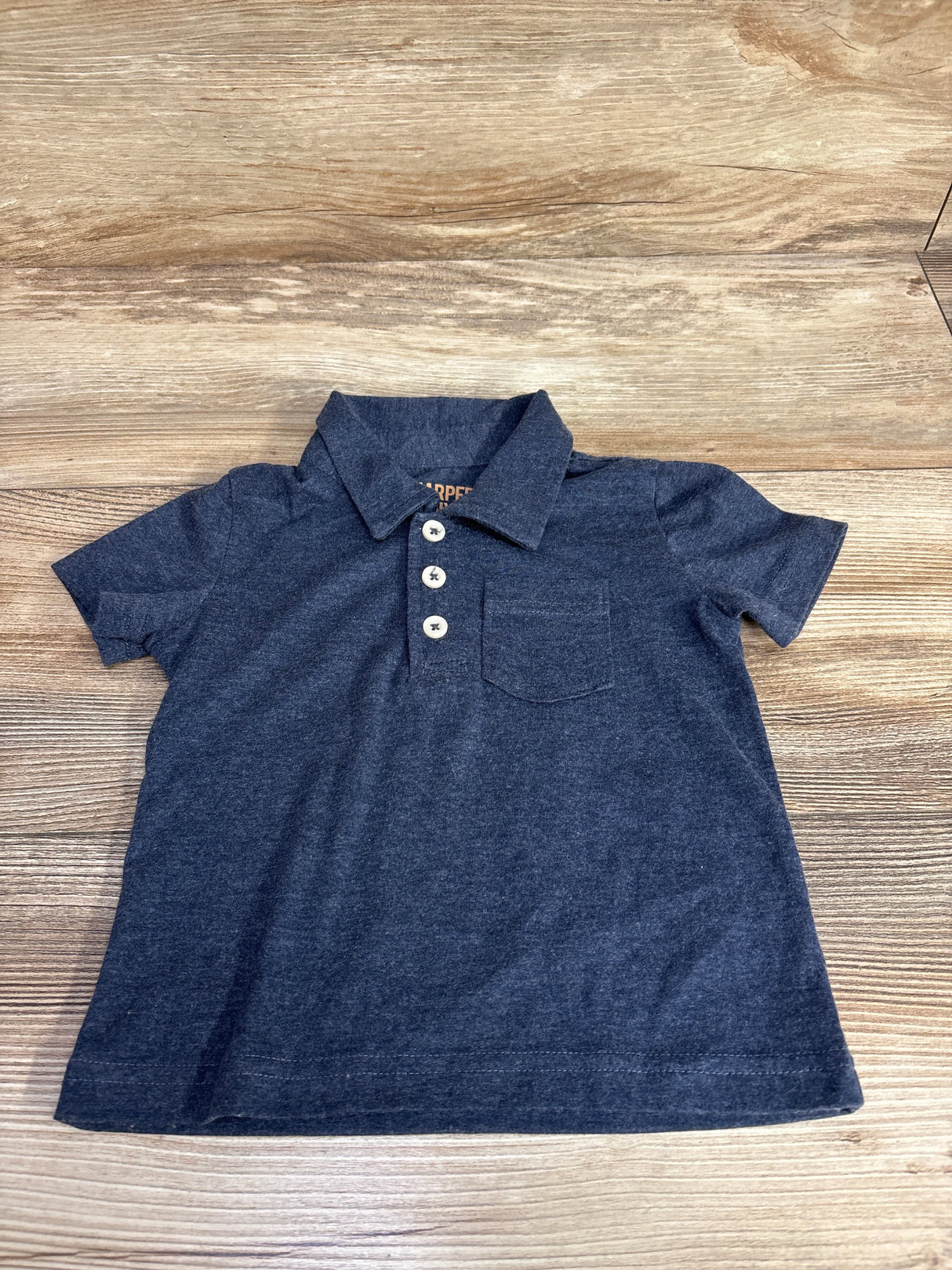 Navy blue toddler polo shirt with buttons and chest pocket on wood background
