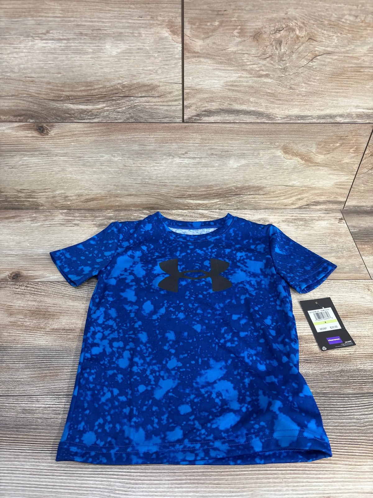 Flat lay of boys’ Under Armour short-sleeve shirt in blue splatter with black logo on wood floor