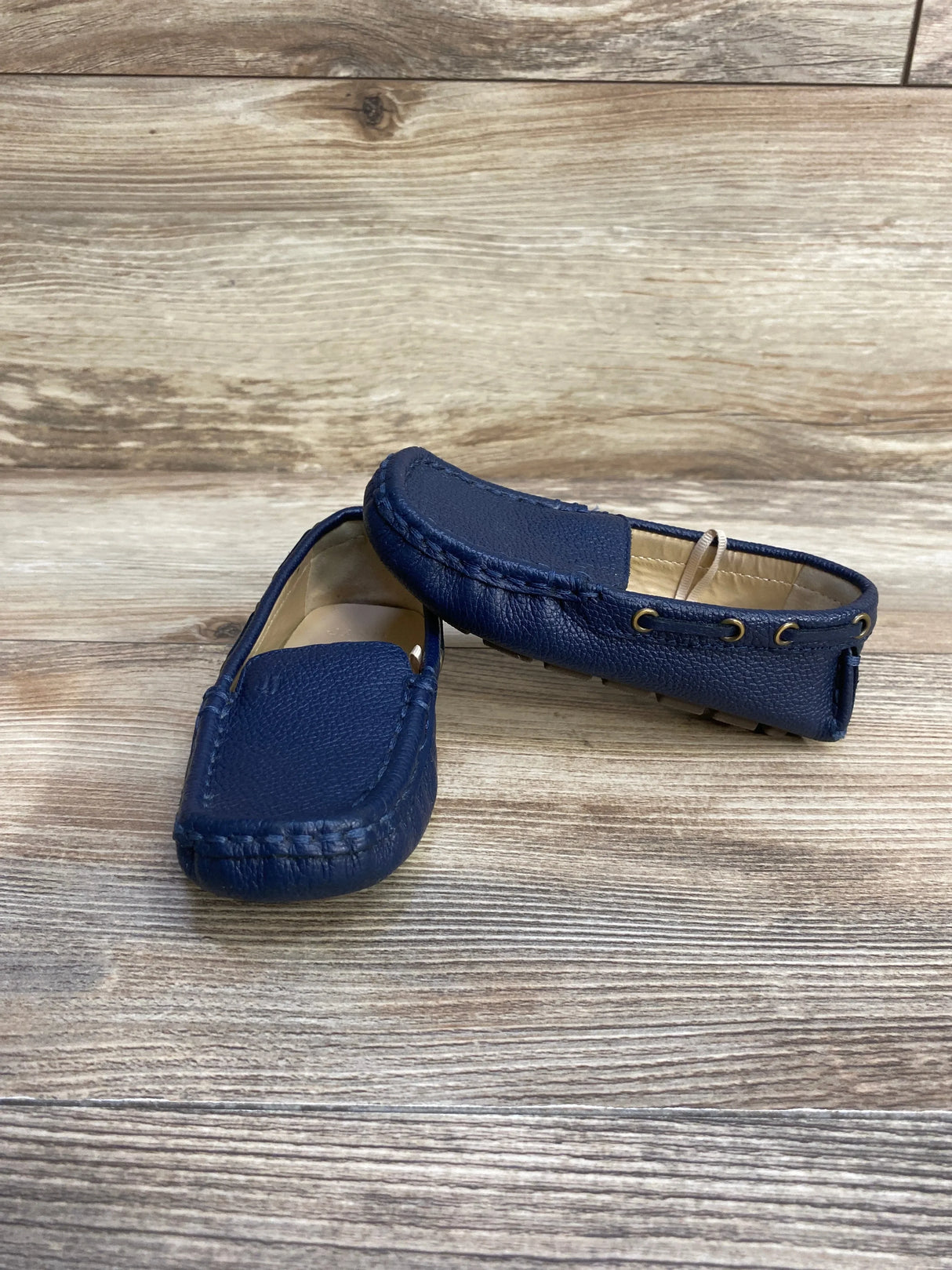 Angled view of Janie and Jack navy leather driving shoes with moc-toe stitching, eyelets and rubber nub sole on wood background