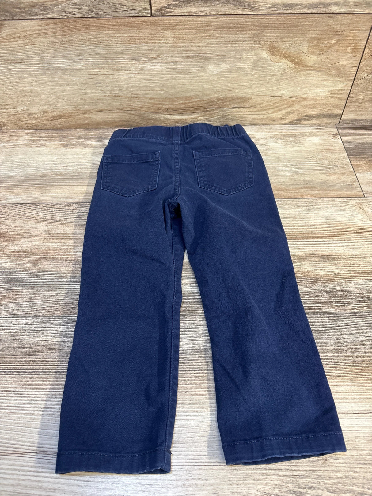 Back view of navy toddler skinny twill pants with elastic drawstring waist and back patch pockets on light wood background