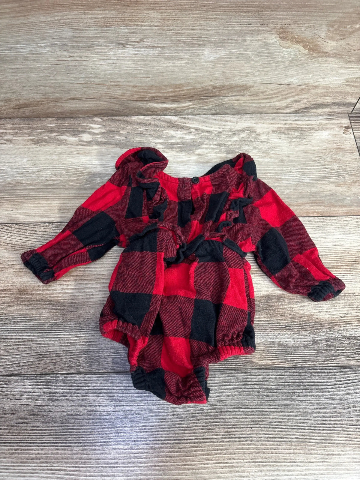 Red and black plaid long-sleeve baby onesie with ruffle detailing on wooden background