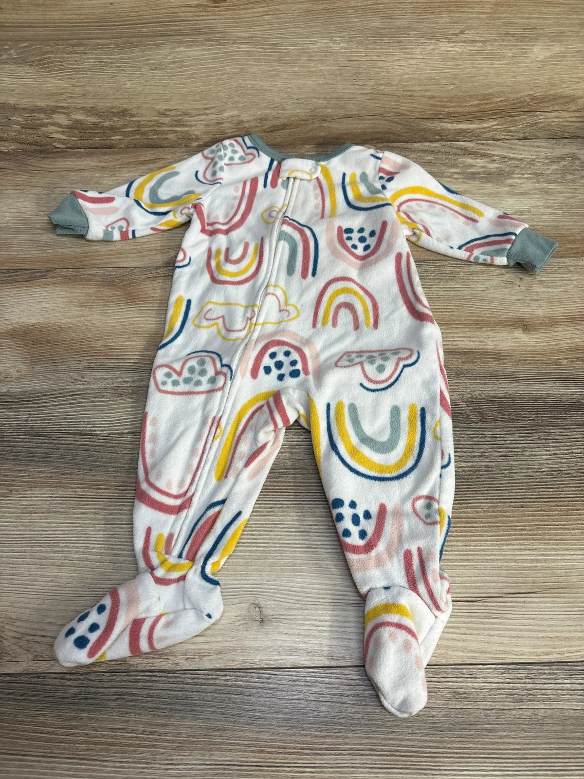 Flat lay of Carter’s white blanket sleeper with rainbow and cloud print, front zipper and footed legs on wood background
