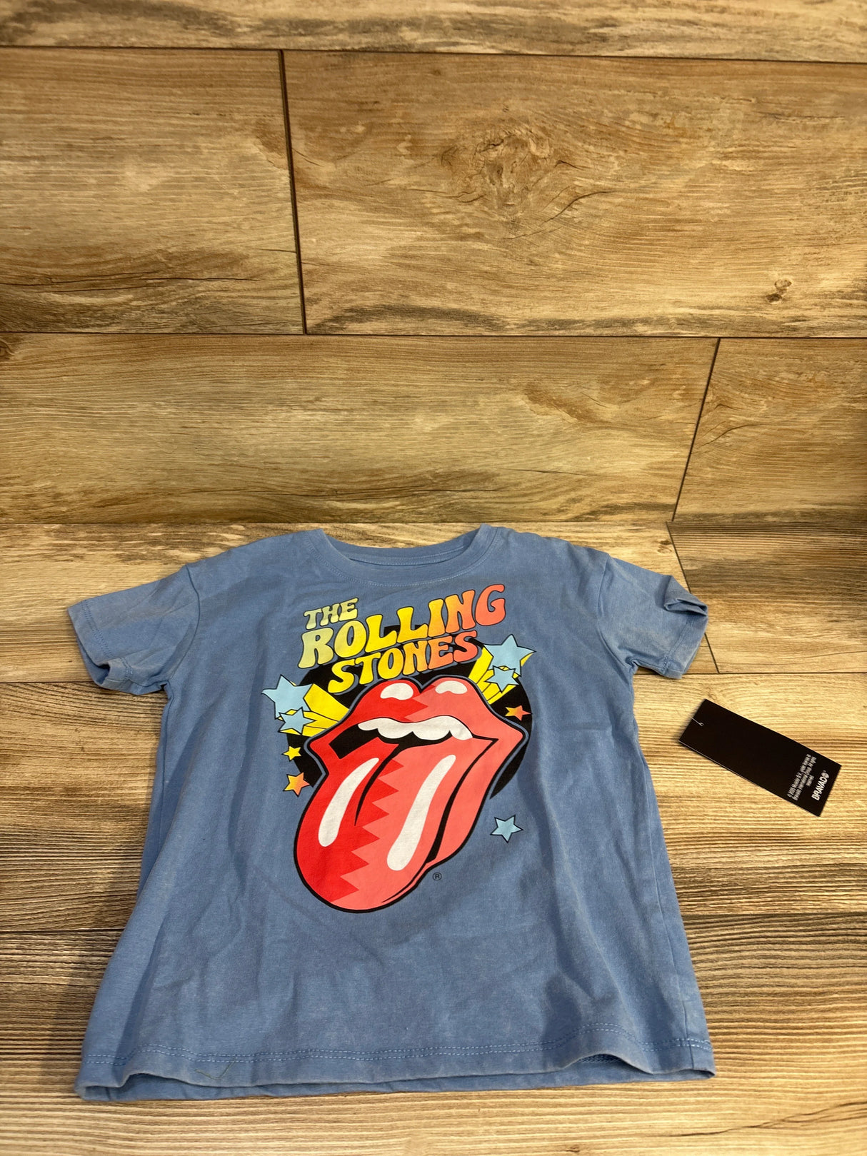 Front view of size 5T blue Rolling Stones tee with large red tongue graphic, laid flat on wood background