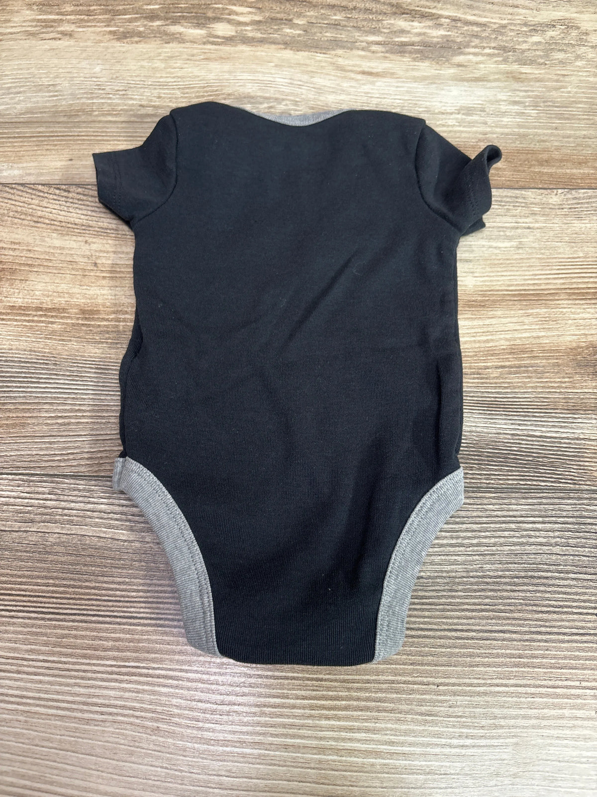 Black baby bodysuit with grey trim, size 0-6m, laid flat on a wooden surface.