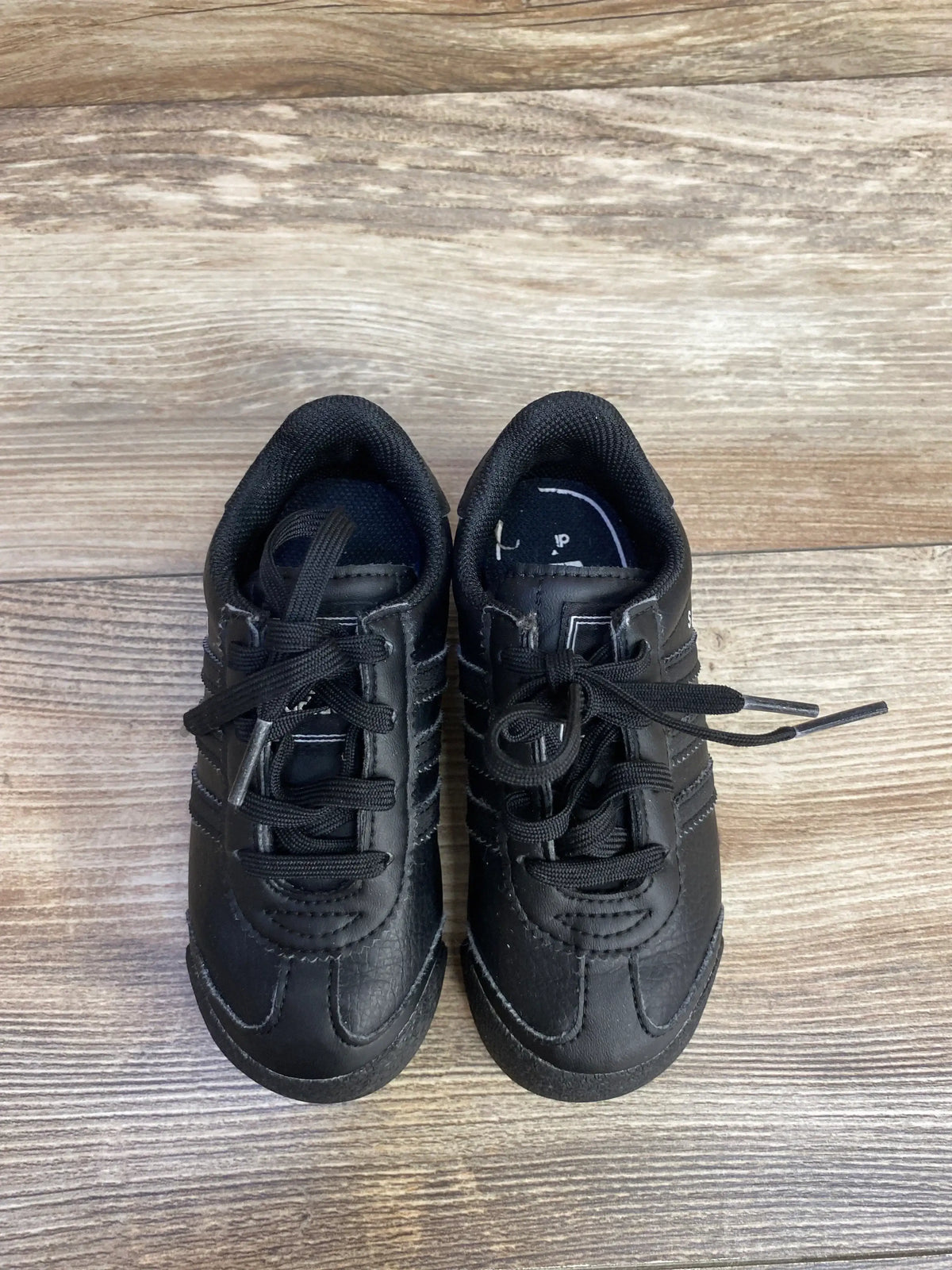 Top view of Adidas Samoa toddler sneakers size 8C showcasing black leather upper, three stripes and laces on wood floor