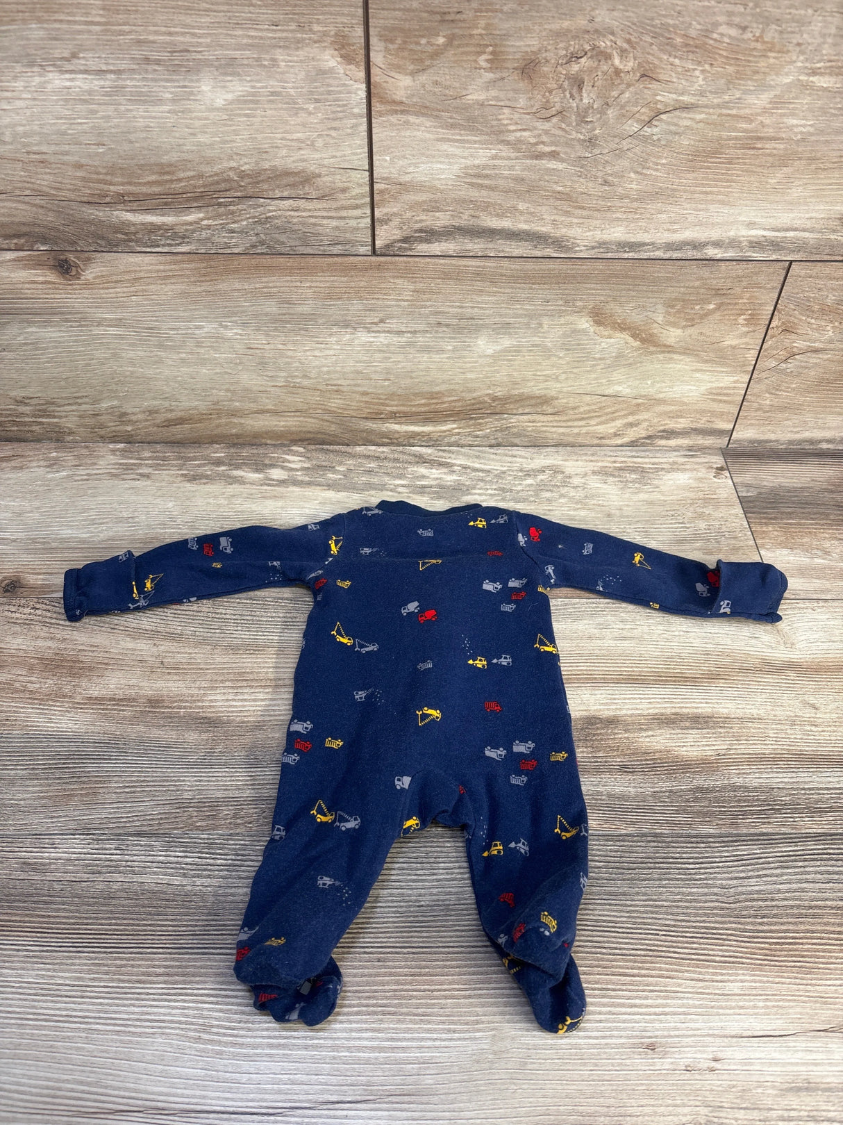 Top-down view of Simple Joys navy newborn truck sleeper with an all-over construction truck print on wood-grain background