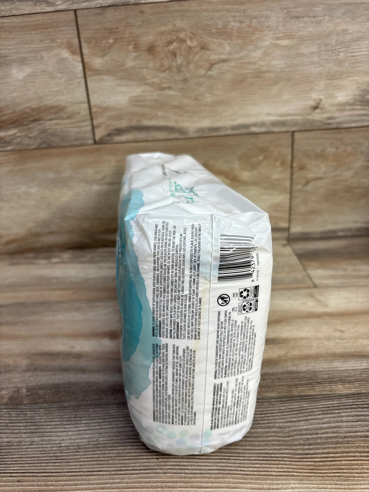 Side view of a sealed pack of disposable baby diapers on wood floor background
