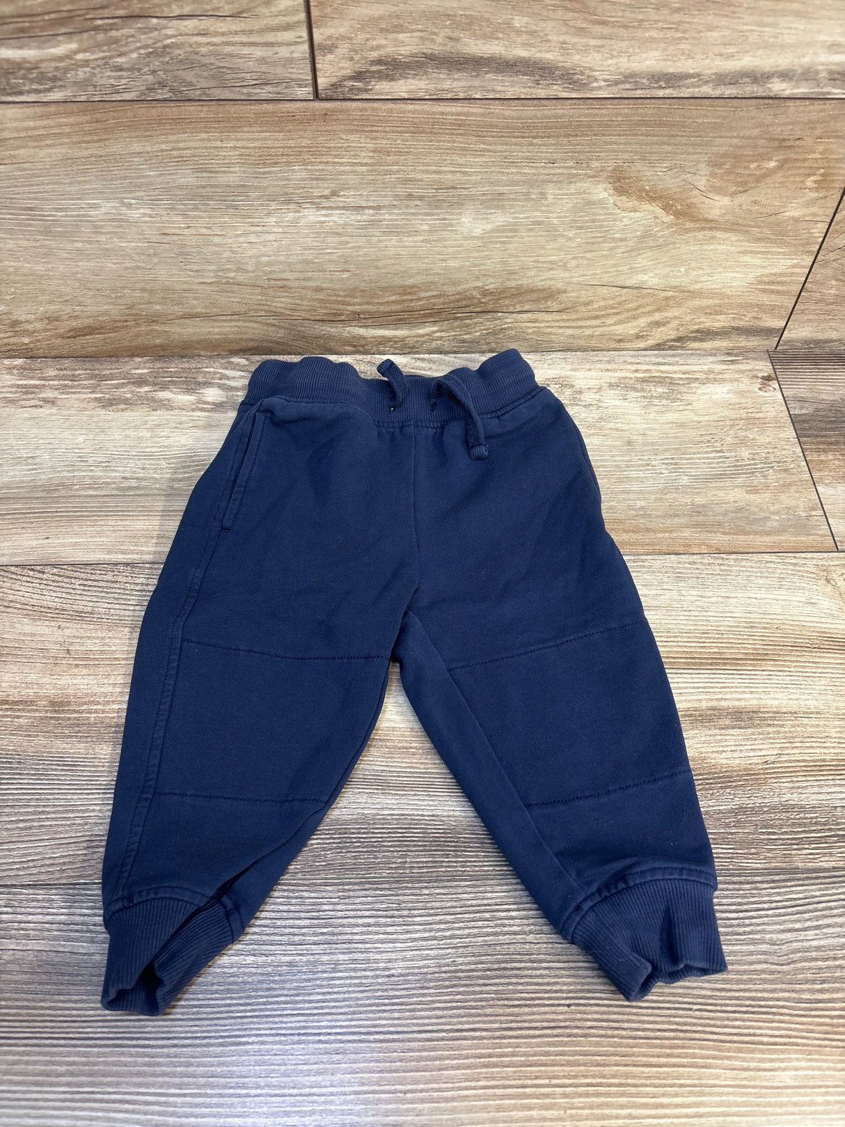Navy blue kids joggers with drawstring waist, laid flat on wood floor for resale