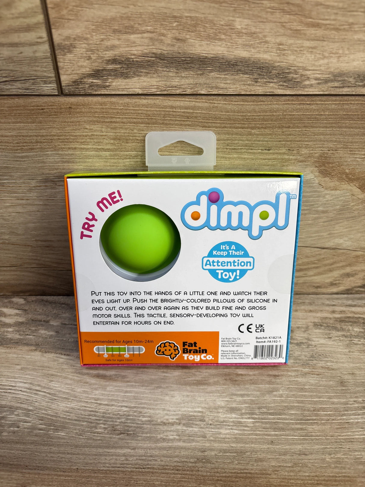 Front view of Fat Brain Toys Dimpl packaging showing green silicone pop bubble, dimpl logo and Try Me text on wood background