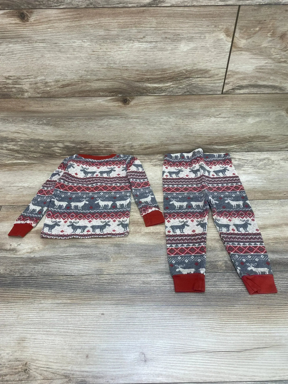 Top-down of Children's Place 2-piece Fair Isle pajama set 9-12m showing red cuffs and reindeer pattern on light wood floor