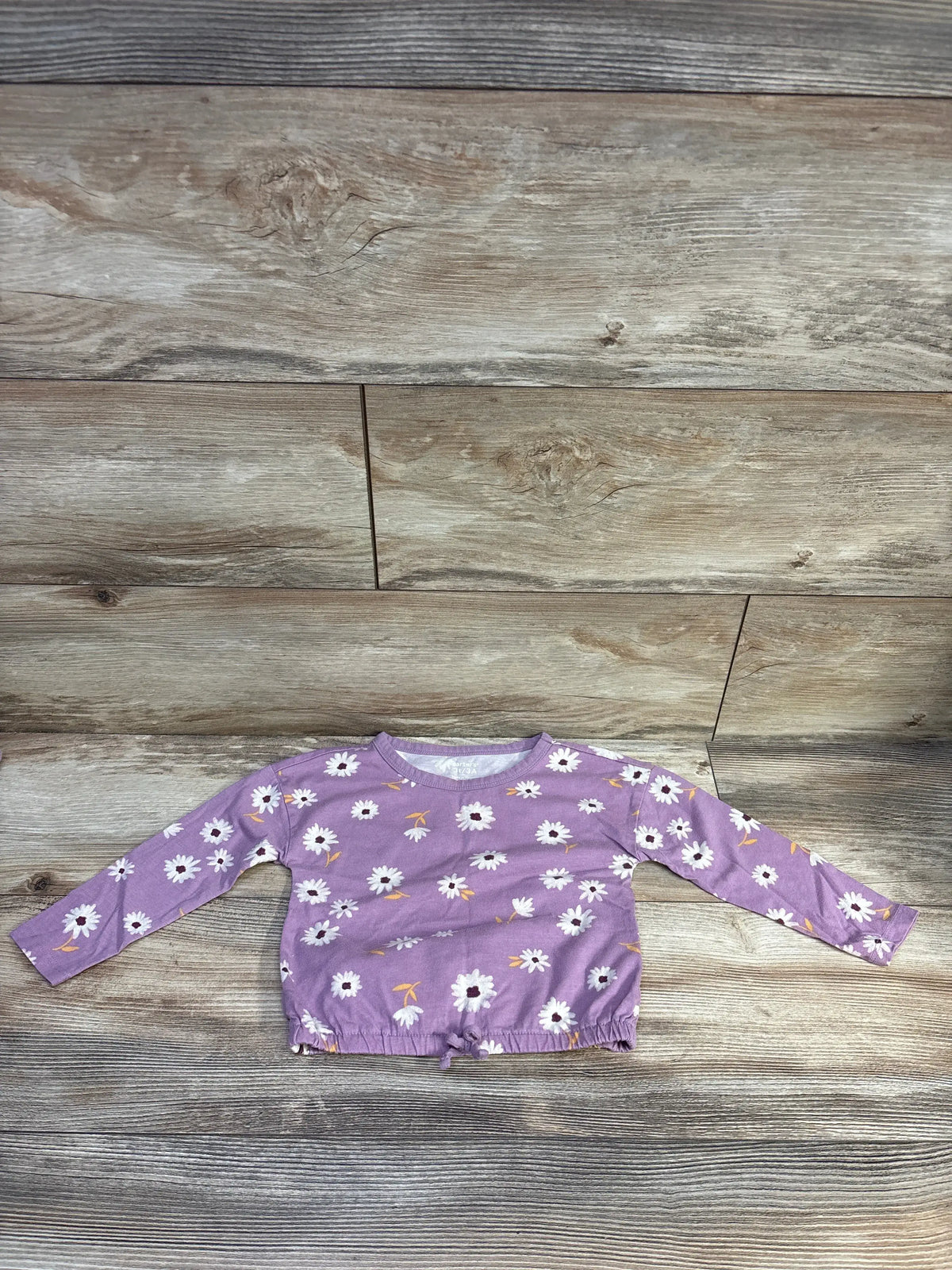 Carter's purple long sleeve toddler shirt with white floral print on a wooden background
