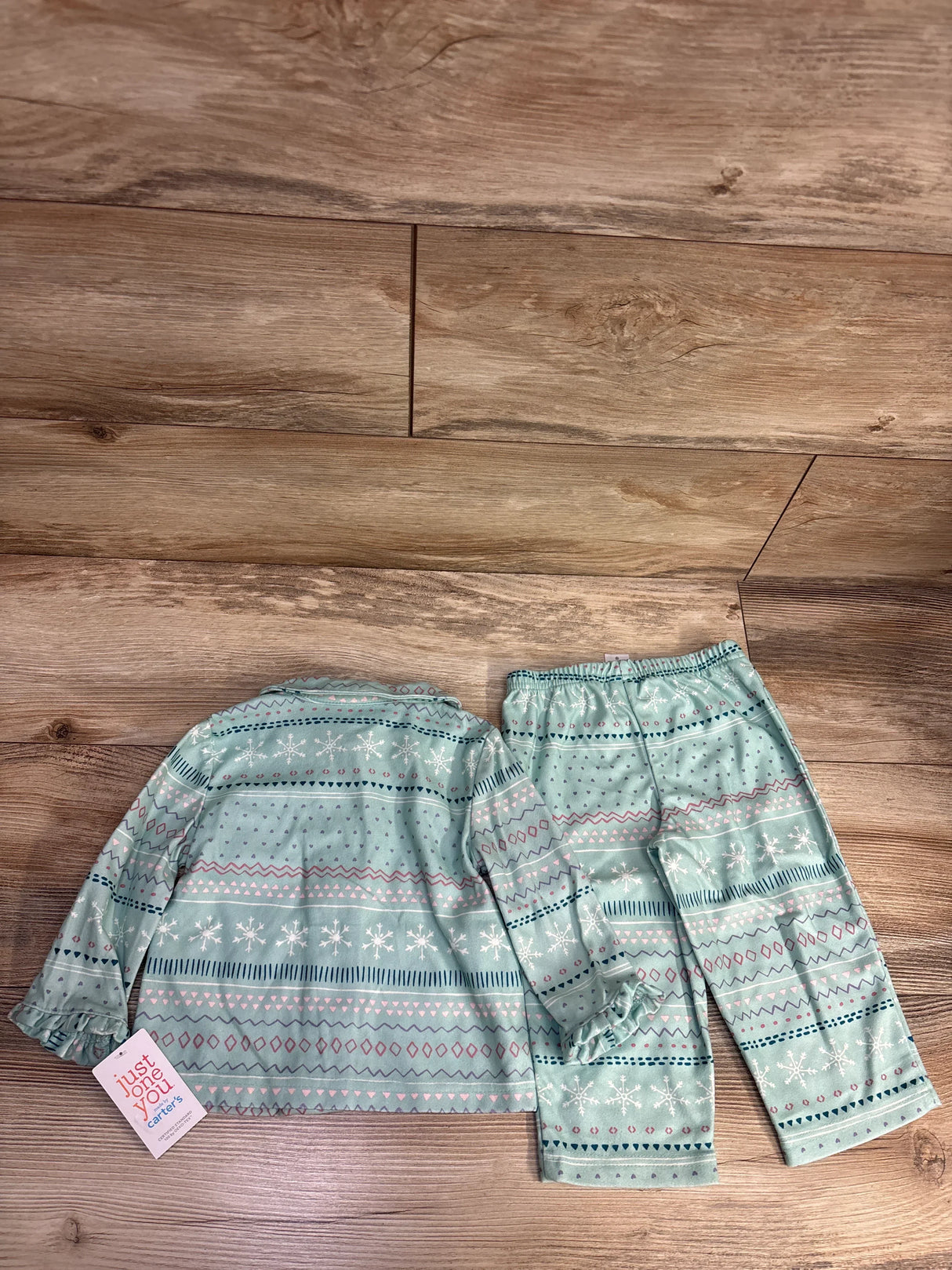 Flat lay of mint green toddler pajama set with fair isle snowflake print and hangtag on wood plank floor