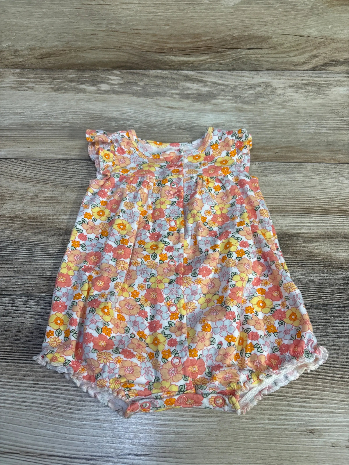 Front view of Carter's white floral shortie romper (3M) showing ruffled cap sleeves, snap crotch, lace-trim elastic legs on wood background
