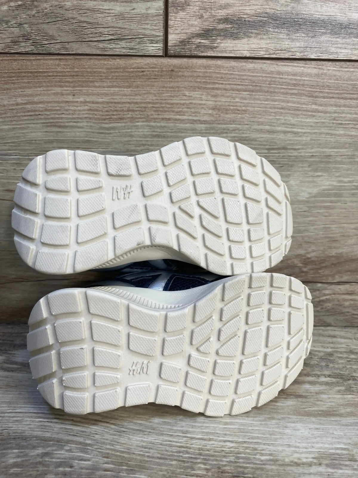 Kids athletic shoes with white rubber soles and grid tread on wood floor