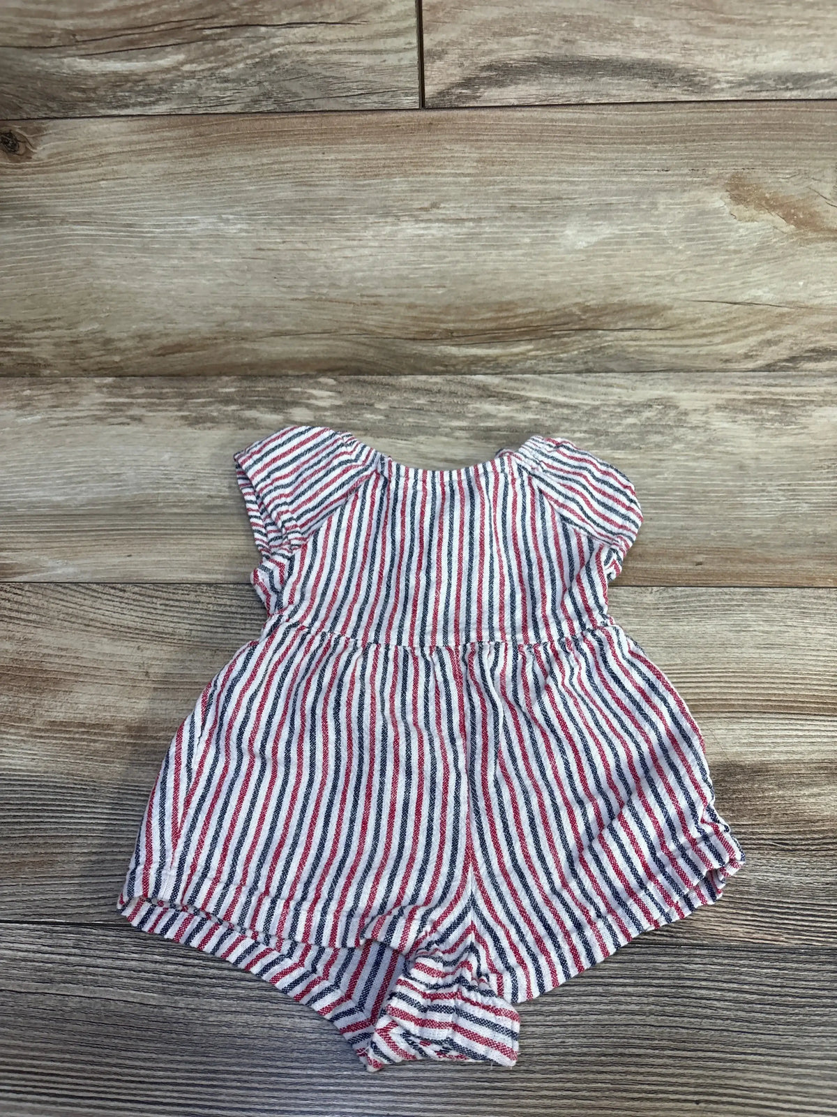Flat lay of Old Navy infant romper with red and navy stripes, flutter sleeves, gathered waist, and elastic leg openings on wood floor