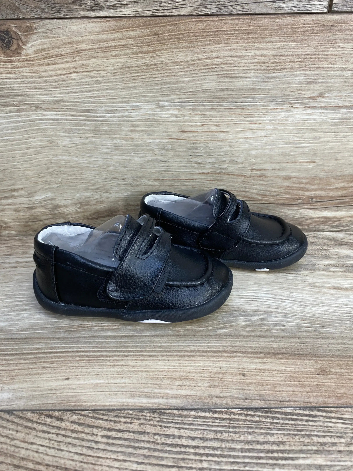 Side view of Pediped Charlie toddler loafers, black leather with Velcro strap and rubber sole, size 5.5C on wood background