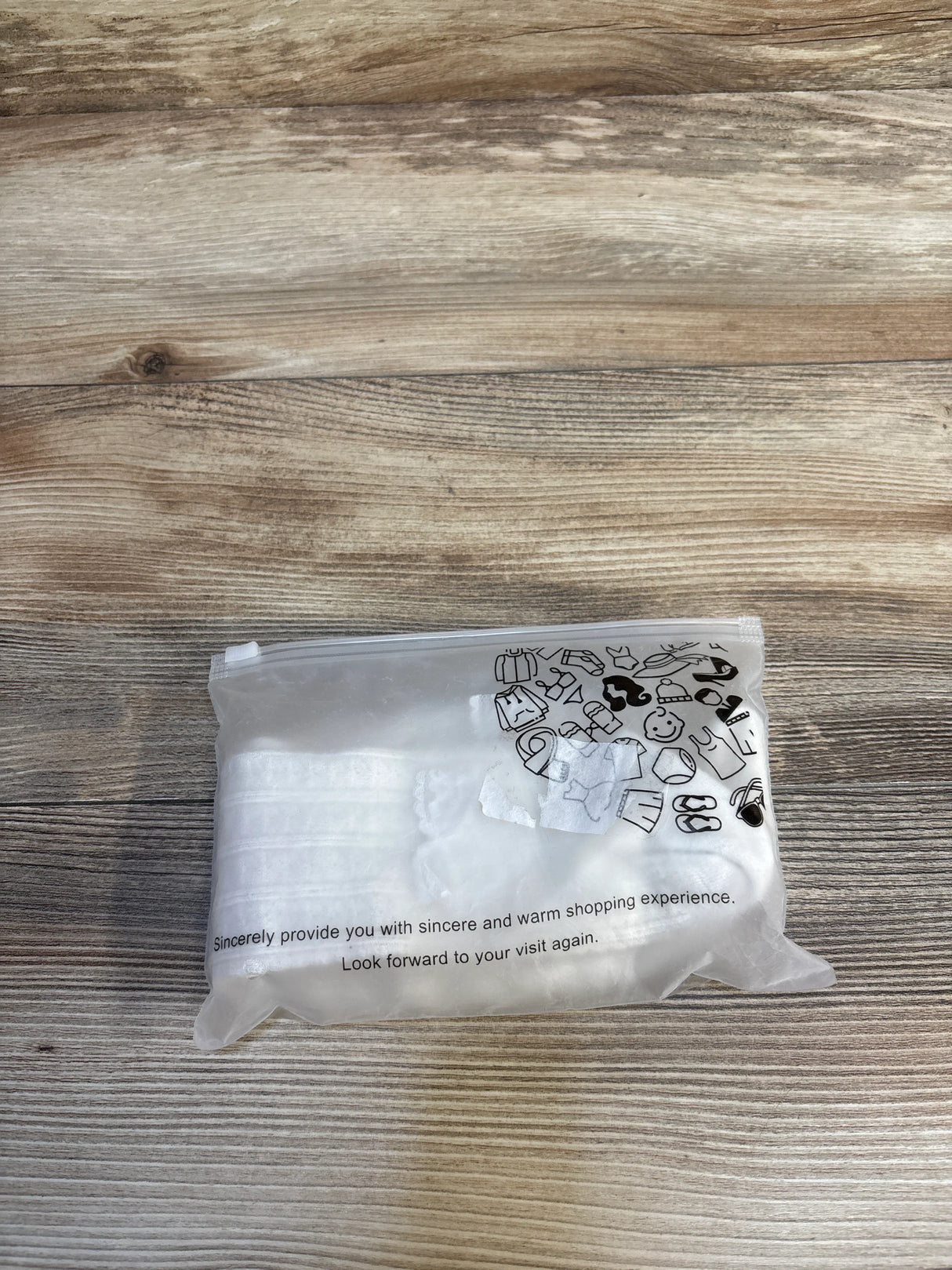 Clear plastic bag with baby items icons, placed on wooden surface, for kids and maternity resale shopping.