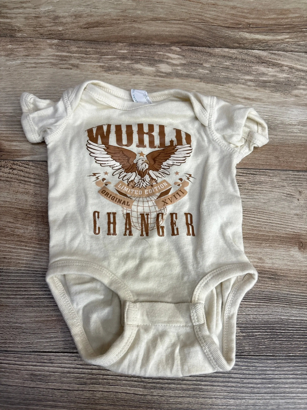 Cream baby onesie with brown eagle graphic and text 'World Changer' on wooden background