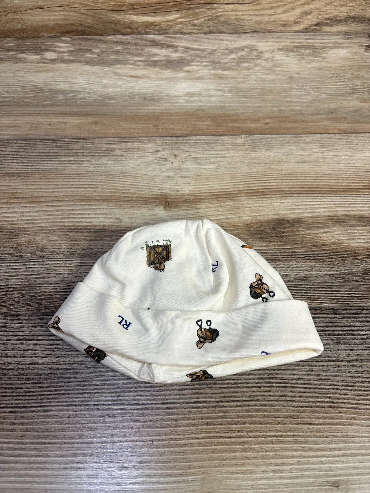 Front view of Ralph Lauren ivory fold-over cap showcasing its gentle cuff and printed motifs on a wood-grain background
