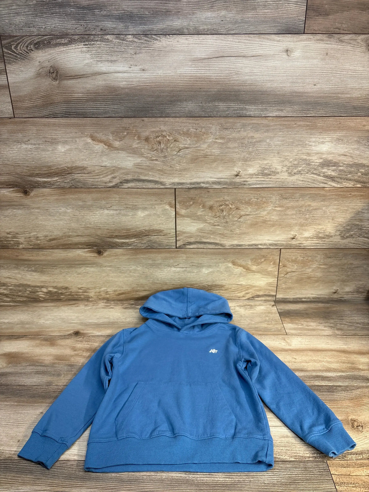 Blue kids hooded sweatshirt with front pocket, long sleeves, laid on wood background