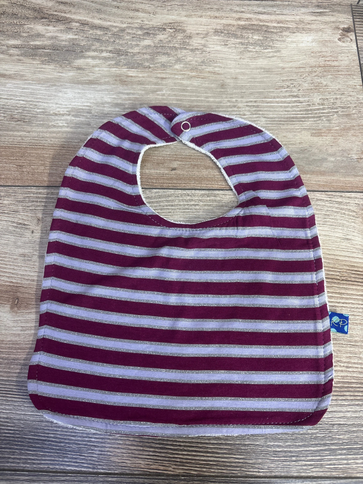 Striped baby bib with purple and silver horizontal lines on wooden floor background