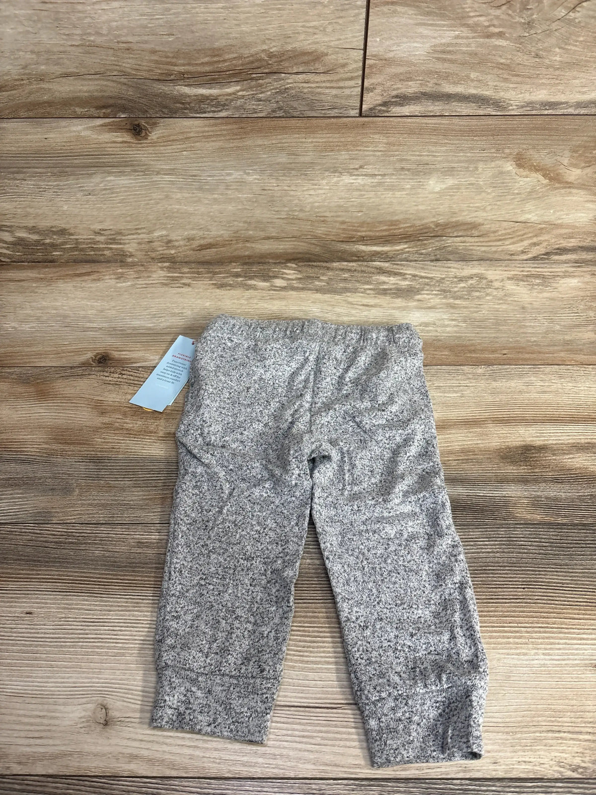 Gray speckled children's pants laid flat on wood surface with clothing tag attached
