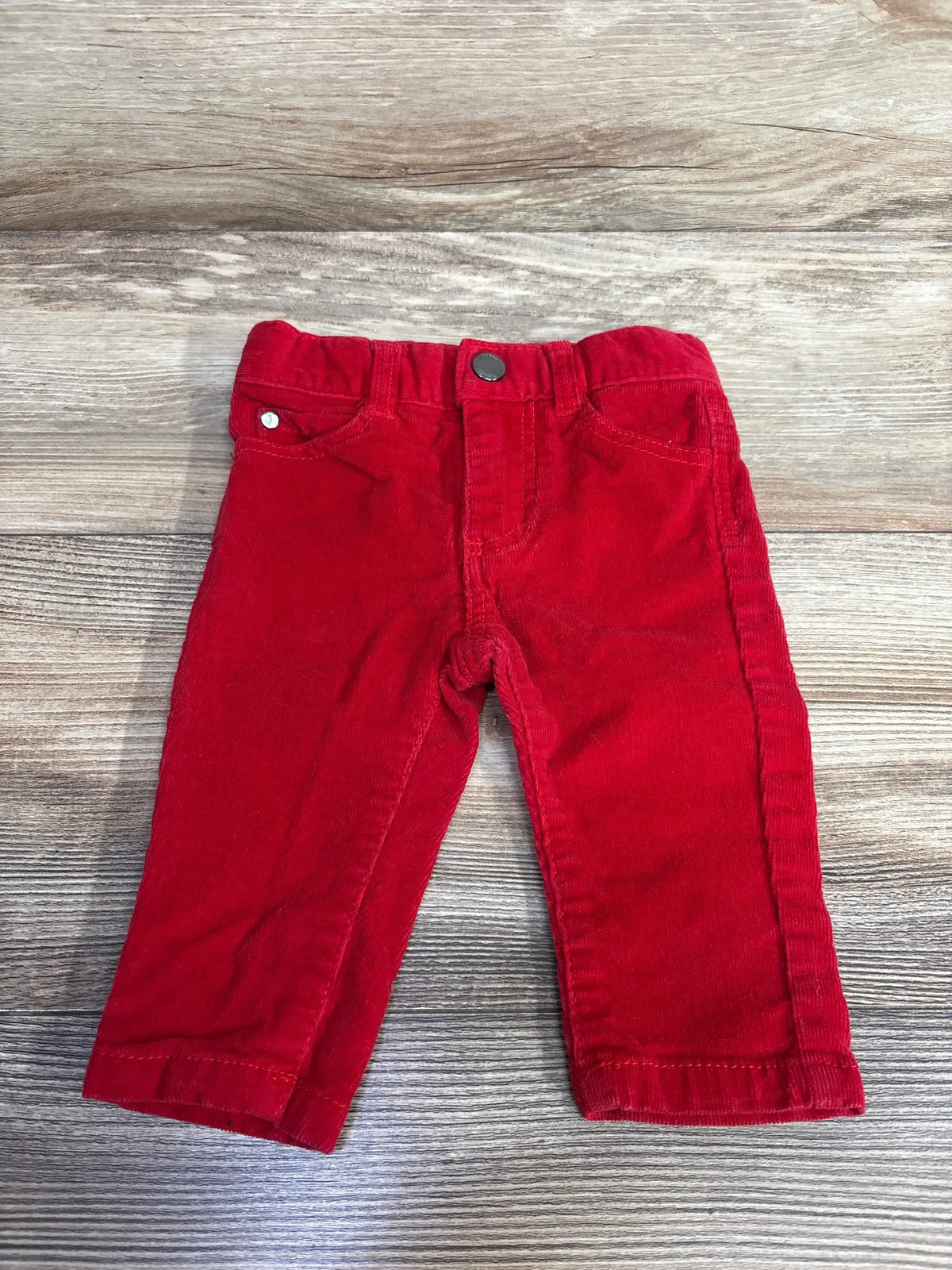 Front view of Jacadi Paris velour baby pants size 3-6 months showing red ribbed velour fabric, button waist and front pockets on wooden background